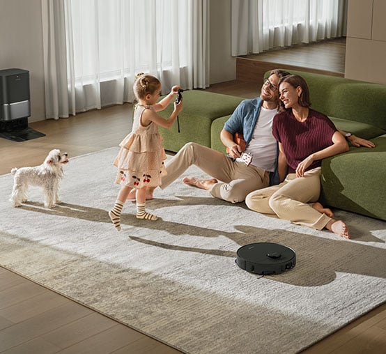 Robot sprzątający Dreame odkurza dywan, na którym przebywają mama, ojciec, dziecko i mały pies